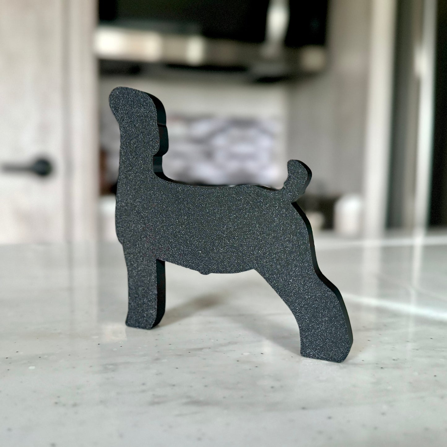 A goat-shaped tabletop decoration made of PLA plastic, featuring a white body with a brown head and ears. The design is outlined in black for a bold, clean look. The goat stands on a light-colored countertop, with a modern kitchen in the background, including a stove and tiled backsplash.