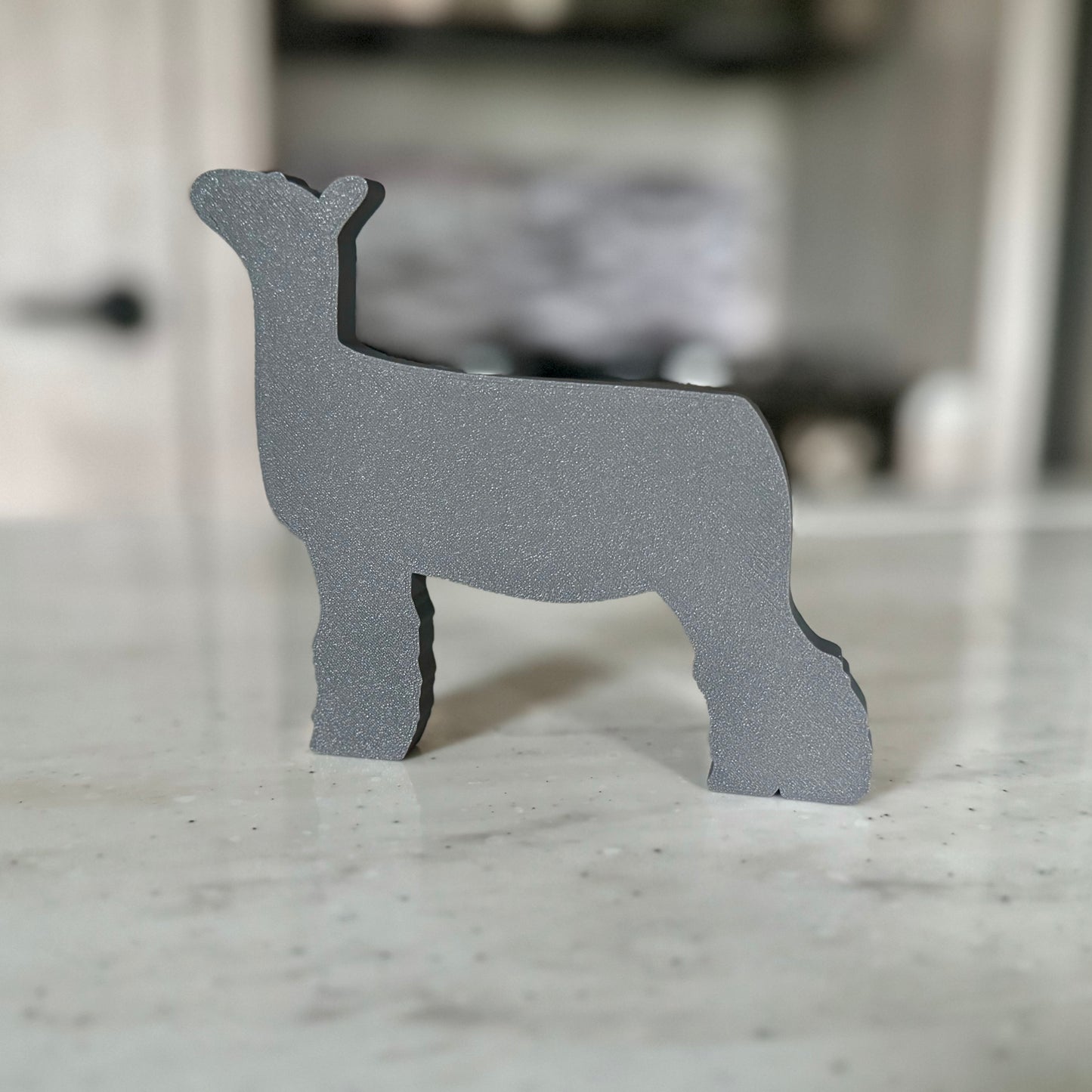 A 3D-printed market lamb figurine featuring a sleek white body, black head, and fluffy black legs, standing on a smooth countertop. The modern, minimalist design showcases clean lines and a show-ready stance, making it a perfect decorative piece for livestock enthusiasts.