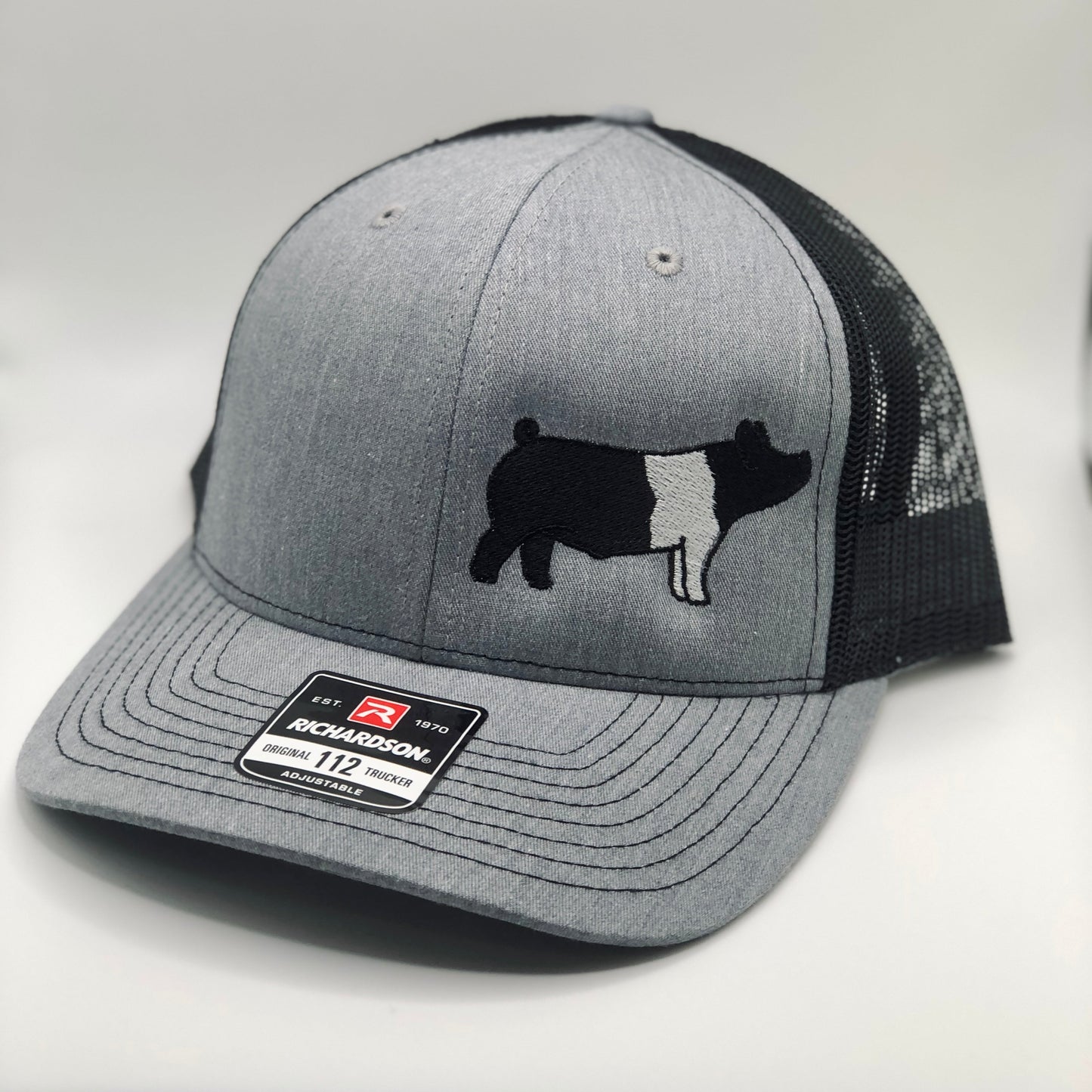 Embroidered pig trucker hat featuring a detailed livestock design. Breathable mesh back with an adjustable snapback closure for a comfortable fit. Perfect for farmers, showmen, and livestock enthusiasts.