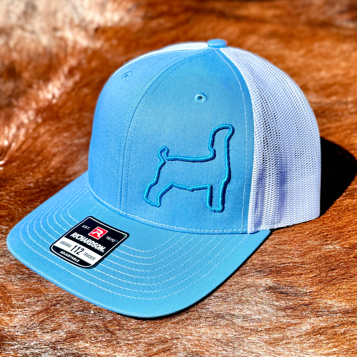 Blue and white trucker cap featuring a raised 3D embroidered outline of a market goat.