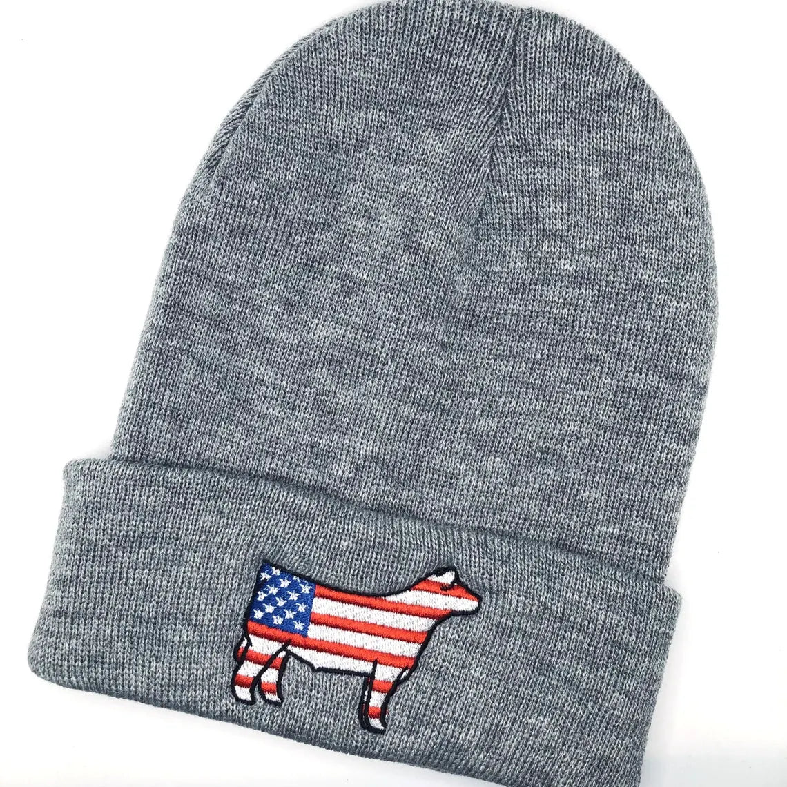 A gray knit beanie with an embroidered show steer patch featuring the American flag design. The steer silhouette is outlined in black, with red and white stripes on the body and a blue field with white stars on the front. The beanie has a folded cuff and is laid flat on a white background.