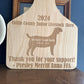 Wooden engraved board with engraved text and a goat silhouette, displayed against a blue wall.