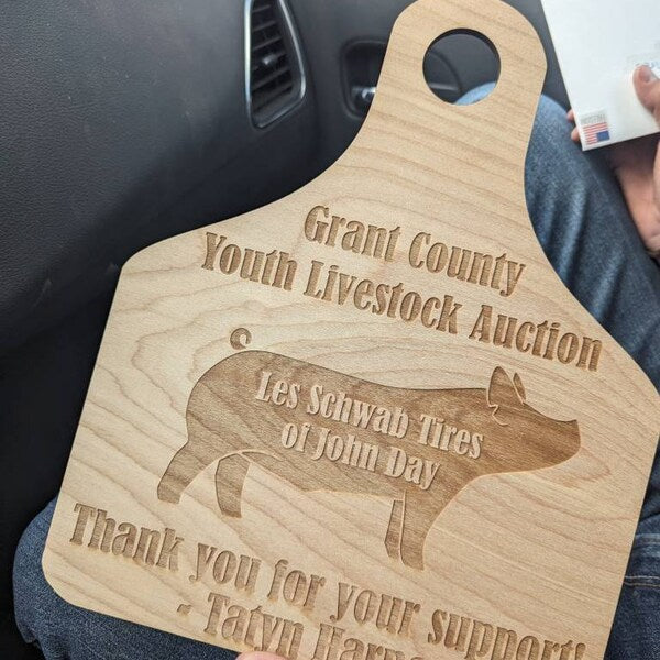 Wooden engraved board with engraved text and pig illustration, held by a person.
