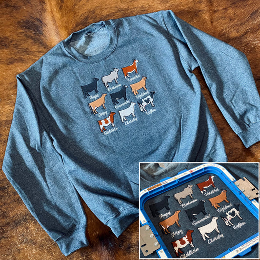 A crewneck sweatshirt featuring detailed embroidered images of various cattle breeds, including Angus, Brahman, Charolais, Chianina, Hereford, Highland, Jersey, Limousin, Shorthorn, and Simmental. The embroidery is arranged neatly on the front, showcasing each breed’s distinct features.