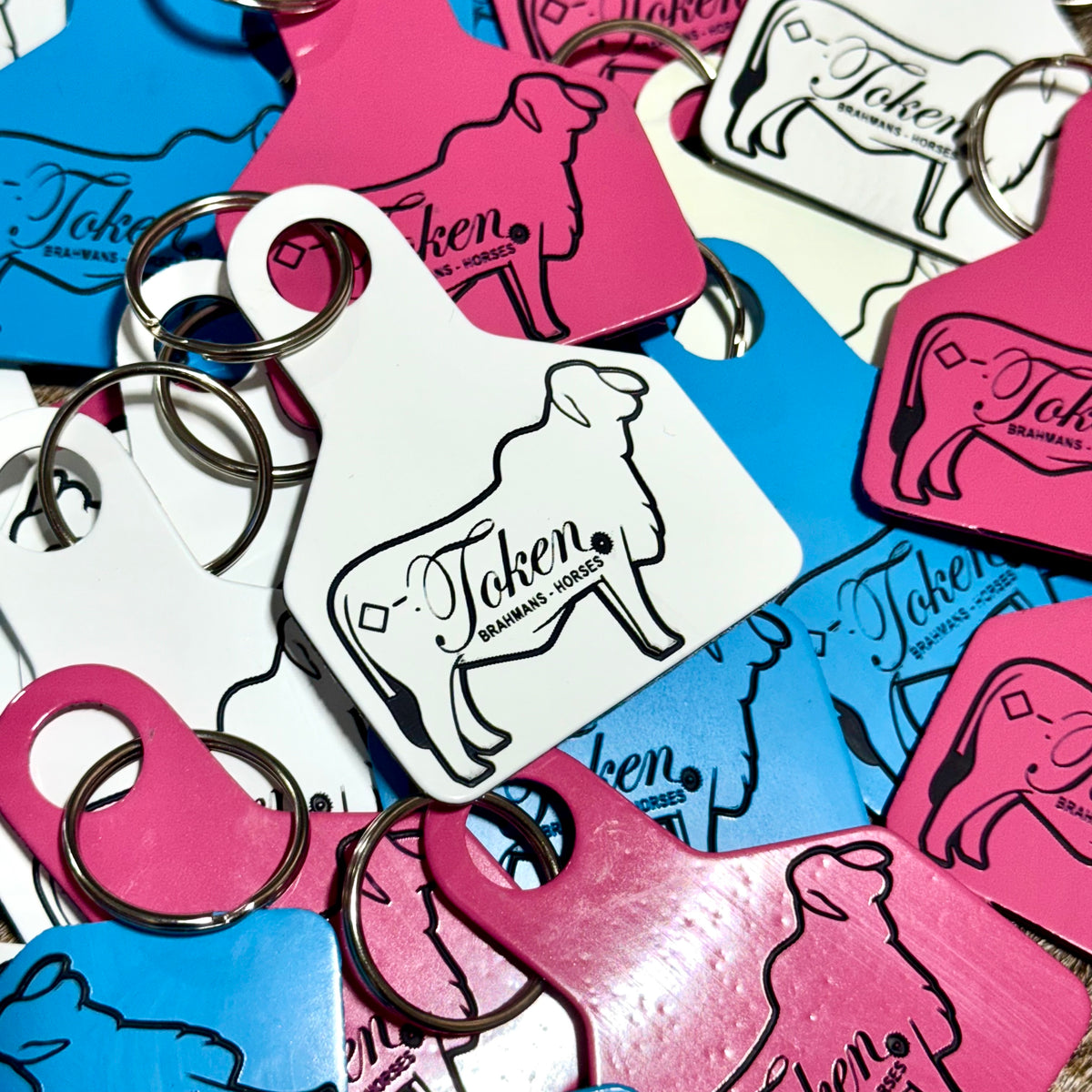 Collection of colorful livestock ear tags being used as keychains with a Brahman heifer and the words 'Token'.