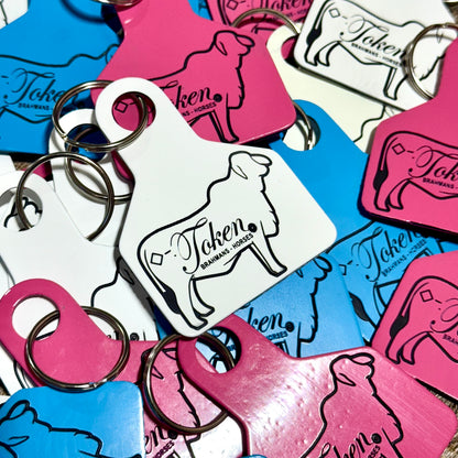 Collection of colorful livestock ear tags being used as keychains with a Brahman heifer and the words 'Token'.