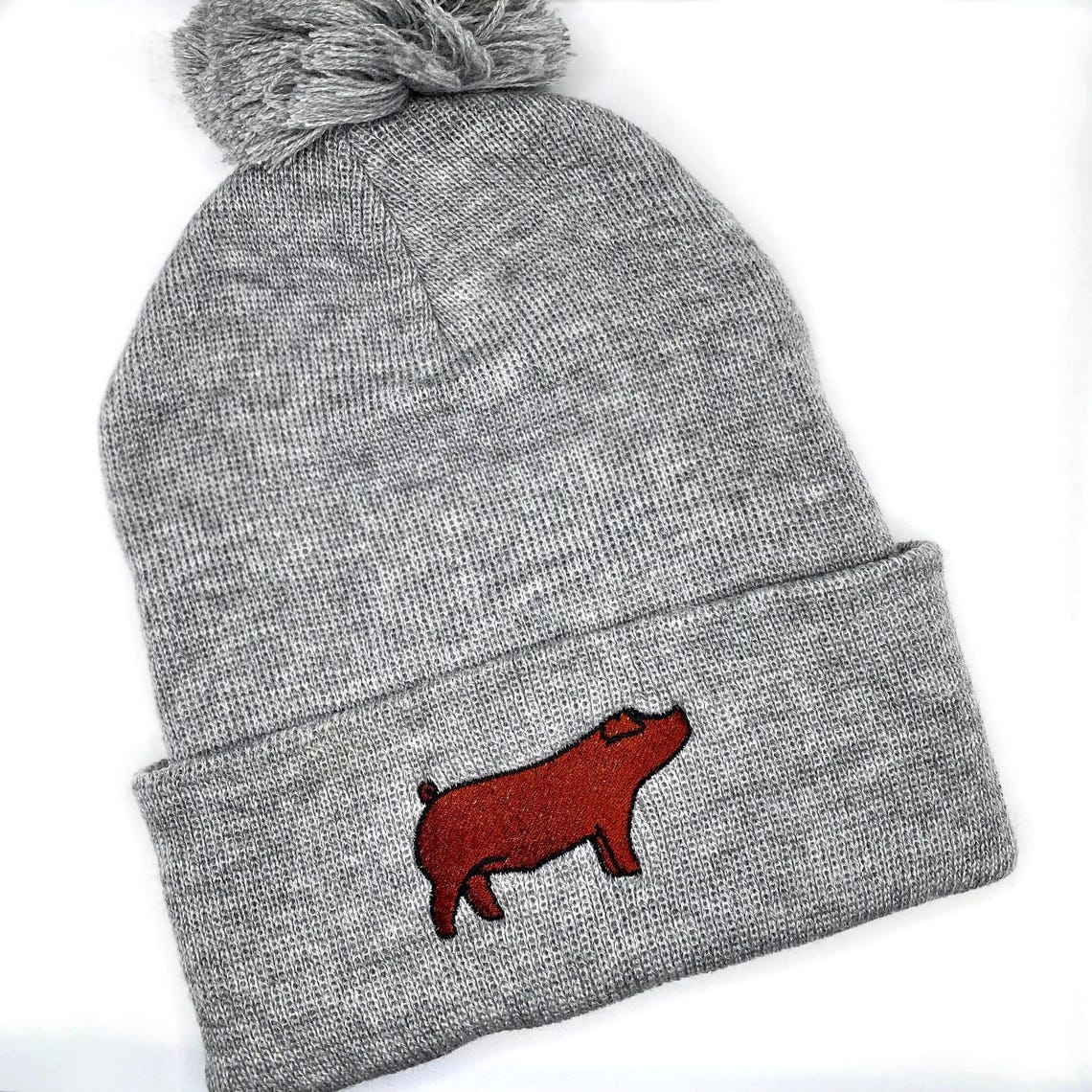 Comfortable and warm winter beanie hat featuring an embroidered red duroc show pig.