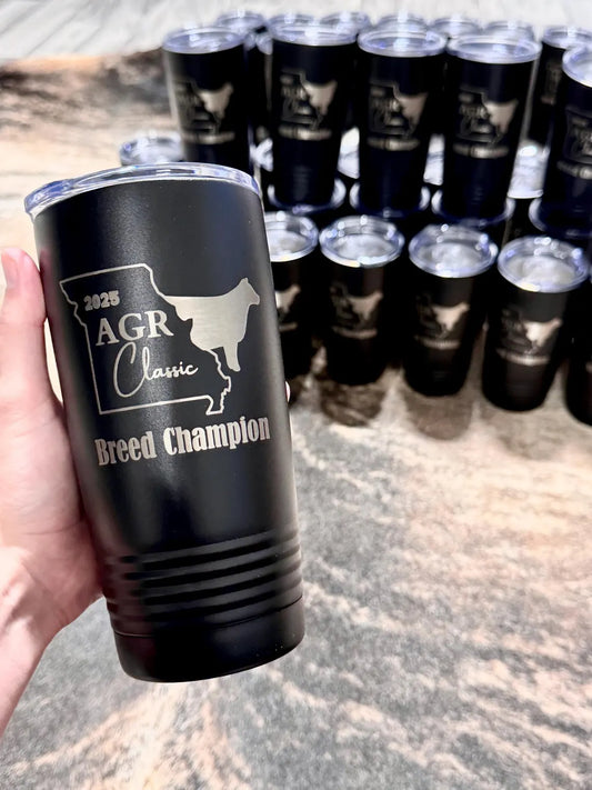 Black tumbler with '2023 AGR Classic Breed Champion' text held by a hand, with more tumblers in the background.
