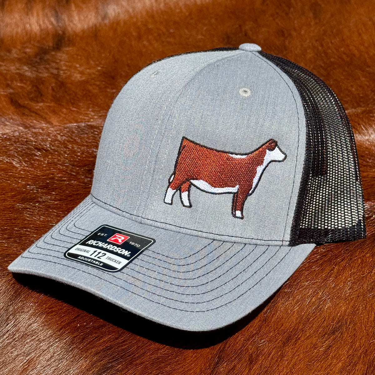 Heather grey and black Richardson 112 hat featuring an embroidered design of a red and white Hereford heifer.