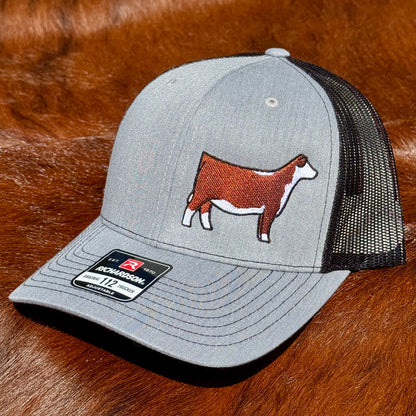 Heather grey and black Richardson 112 hat featuring an embroidered design of a red and white Hereford heifer.