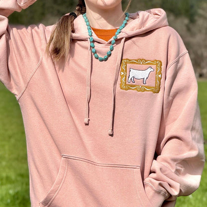 Person wearing a pink hoodie with a show heifer frame design outdoors.