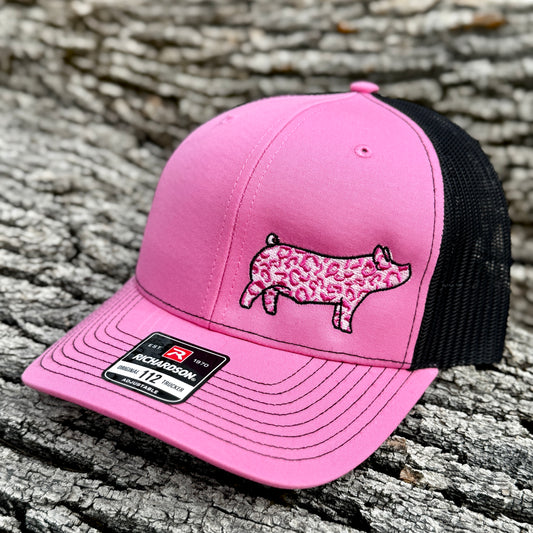 Pink cap with a pink leopard print show pig design on a wooden surface