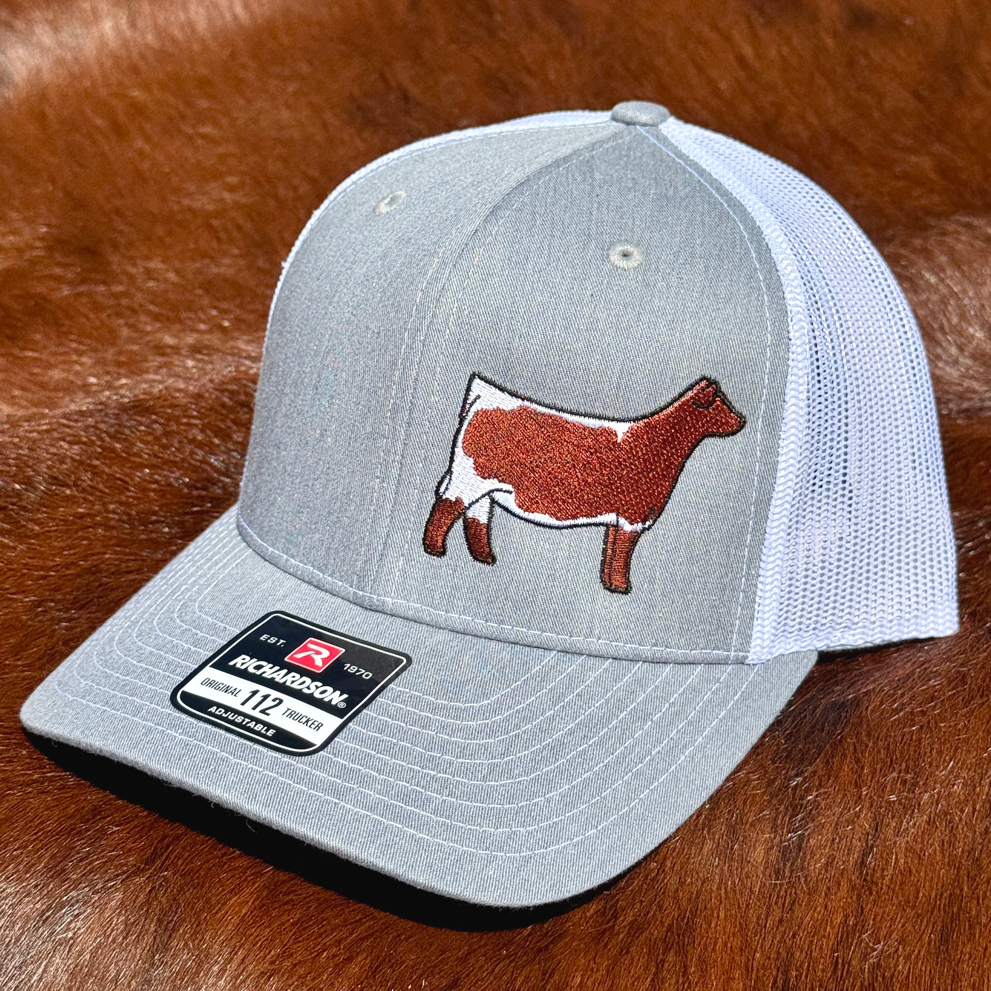 Heather grey and white Richardson 112 hat featuring an embroidered design of a red and white Pinzguaer heifer.