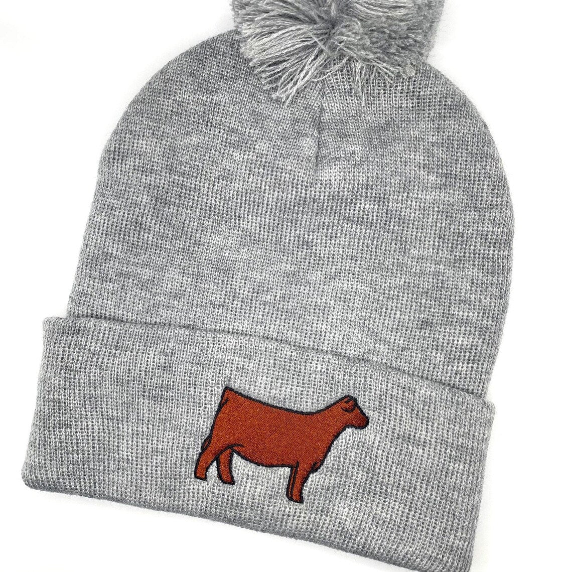 Comfy winter beanie hat with a pompom and high quality embroidery of a Red Angus show heifer. 