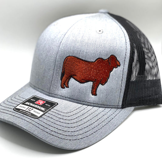 Gray and black Richardson 112 trucker hat featuring an embroidered red Brahman cattle silhouette on the front panel. The hat has a structured fit, mesh back, and an adjustable snapback closure