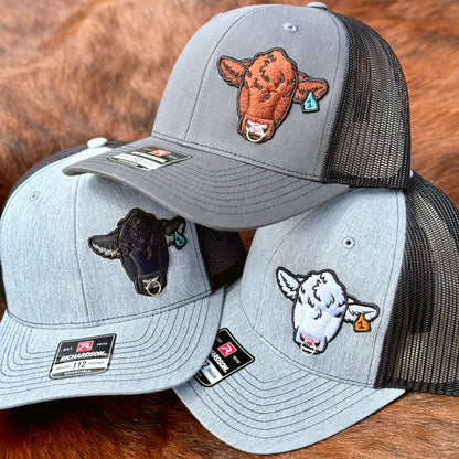 Three Richardson 112 hats featuring embroidered Angus, Red Angus, and Charolais bull heads with real metal rings installed into the bulls noses.