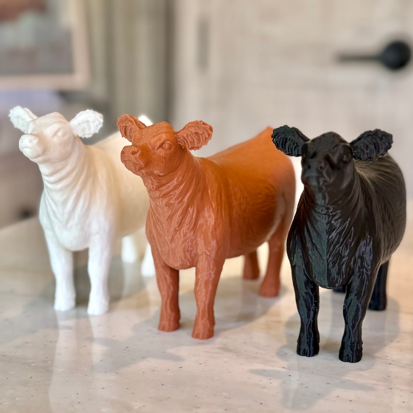 Three show cow figures 3D printed in PLA filament, featuring examples in white, brown, and black.