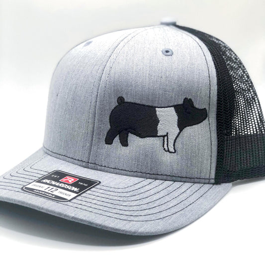 Embroidered pig trucker hat featuring a detailed livestock design. Breathable mesh back with an adjustable snapback closure for a comfortable fit. Perfect for farmers, showmen, and livestock enthusiasts.