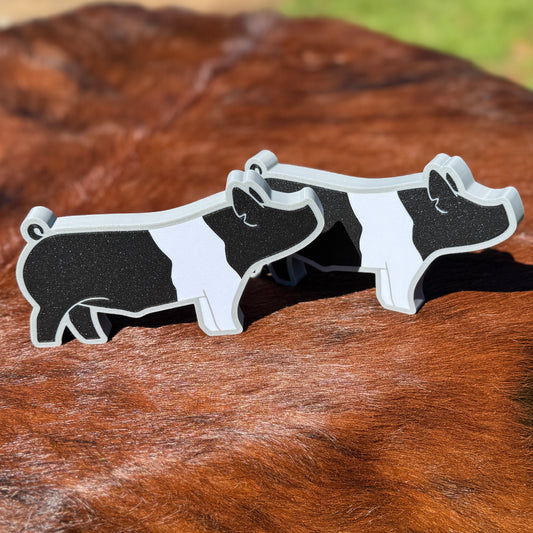 Two standing Hampshire show pig figures outside on a brown brindle cowhide rug.