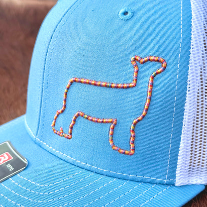 Close up of a blue hat featuring colorful raised 3D embroidery of an outline of a show lamb.