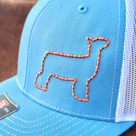 Close up of a blue hat featuring colorful raised 3D embroidery of an outline of a show lamb.