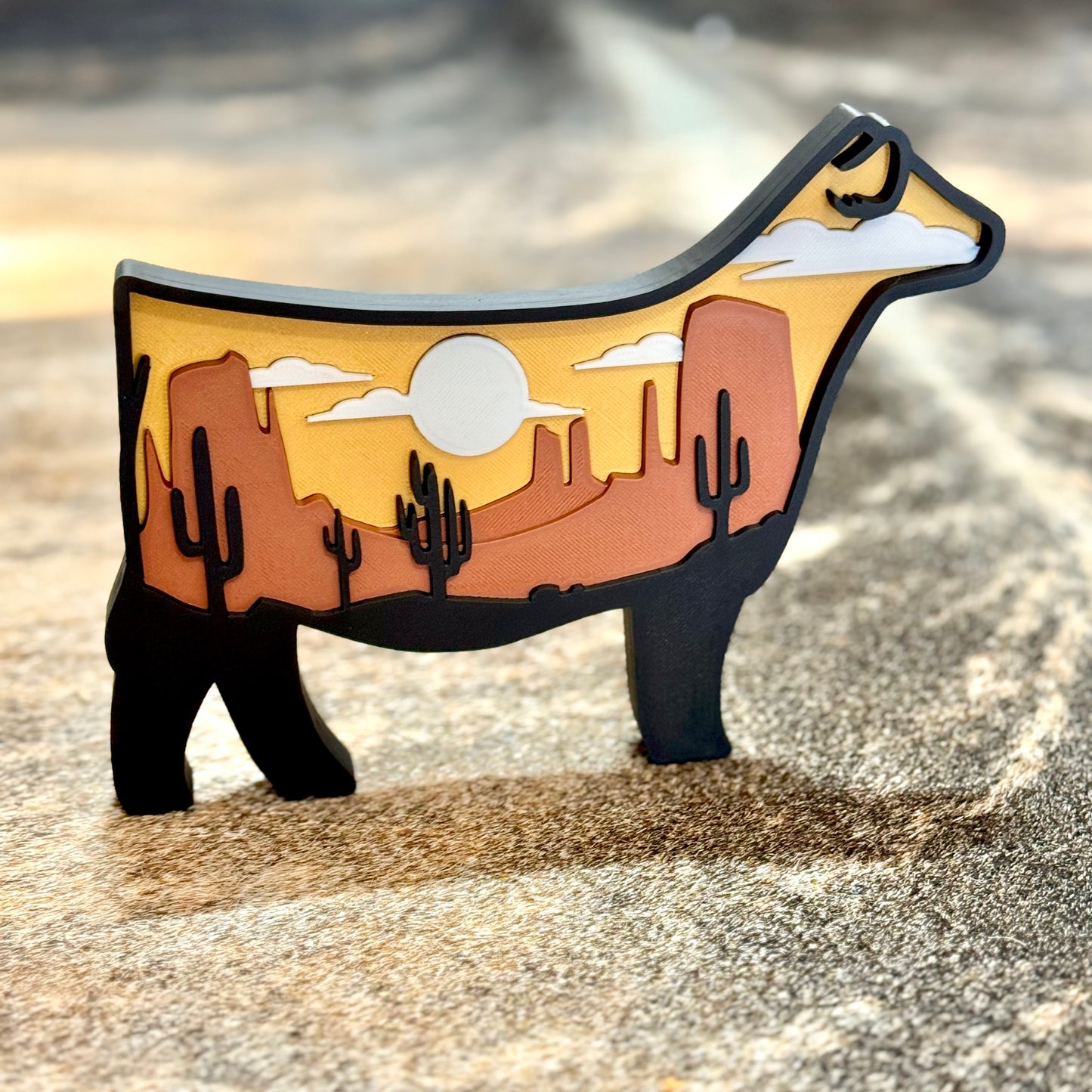 Decorative cow-shaped piece with desert landscape design on a textured surface