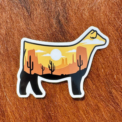 Cow-shaped sticker with desert landscape design.