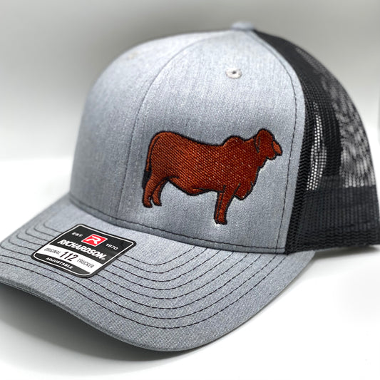 Gray and black Richardson 112 trucker hat featuring an embroidered red Brahman cattle silhouette on the front panel. The hat has a structured fit, mesh back, and an adjustable snapback closure