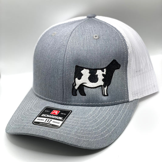 A custom embroidered trucker hat featuring a detailed Shorthorn cow silhouette on the front panel. Available in three color combinations: grey with black mesh, grey with white mesh, and charcoal with black mesh. Designed with a breathable mesh back and an adjustable snapback closure, this hat comes in both adult and youth sizes, making it a perfect fit for livestock enthusiasts of all ages.