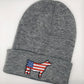 A gray knit beanie with an embroidered show steer patch featuring the American flag design. The steer silhouette is outlined in black, with red and white stripes on the body and a blue field with white stars on the front. The beanie has a folded cuff and is laid flat on a white background.
