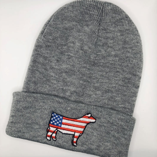 A gray knit beanie with an embroidered show steer patch featuring the American flag design. The steer silhouette is outlined in black, with red and white stripes on the body and a blue field with white stars on the front. The beanie has a folded cuff and is laid flat on a white background.