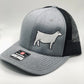 A gray and black Richardson 112 trucker hat with an embroidered white Charolais cow design on the front panel. The hat features a structured front, a curved brim, and a black mesh back for ventilation. A brand sticker is visible on the brim.