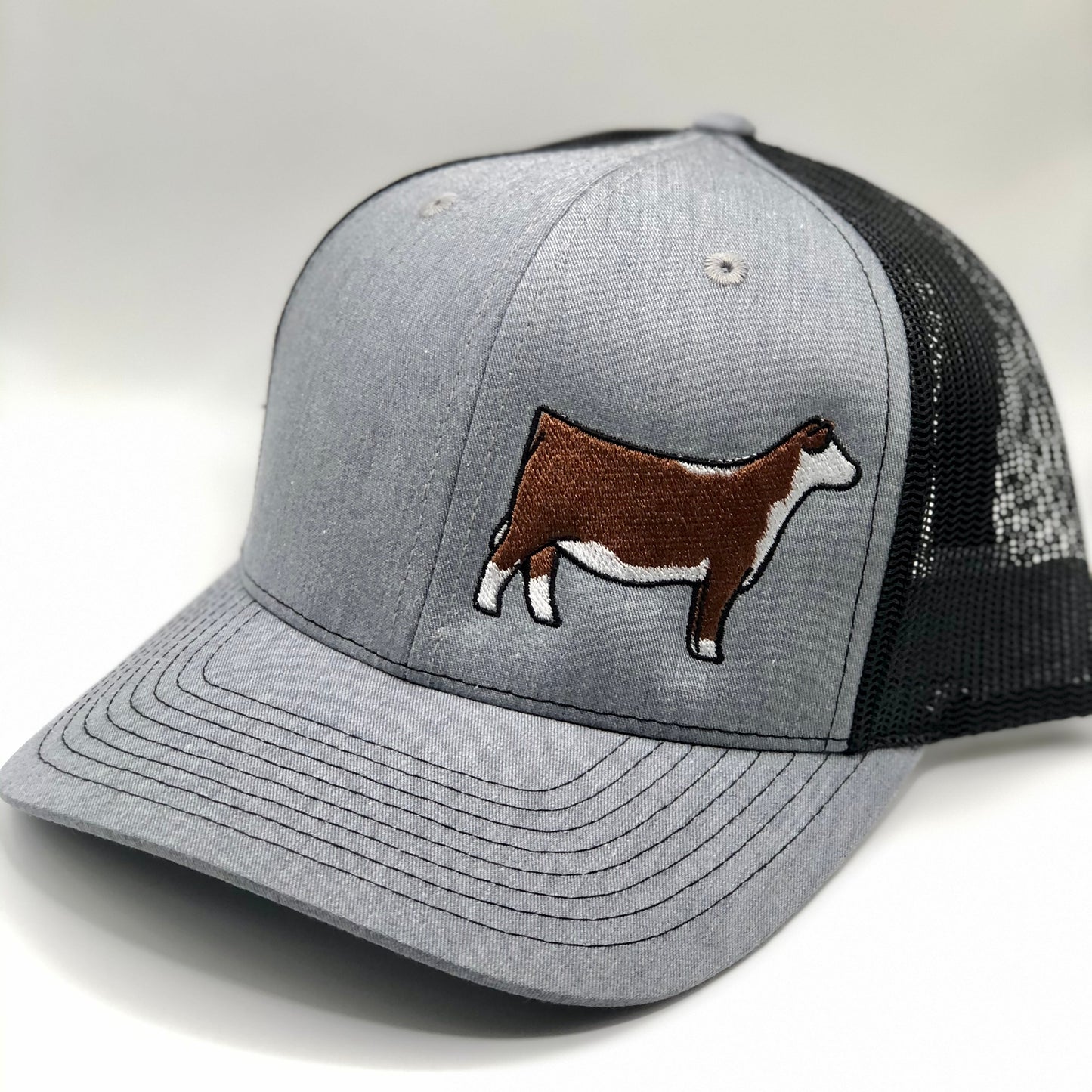 Embroidered Hereford trucker hat featuring a detailed cattle design. Breathable mesh back with an adjustable snapback closure for a comfortable fit. Perfect for ranchers, cattle show enthusiasts, and livestock lovers.